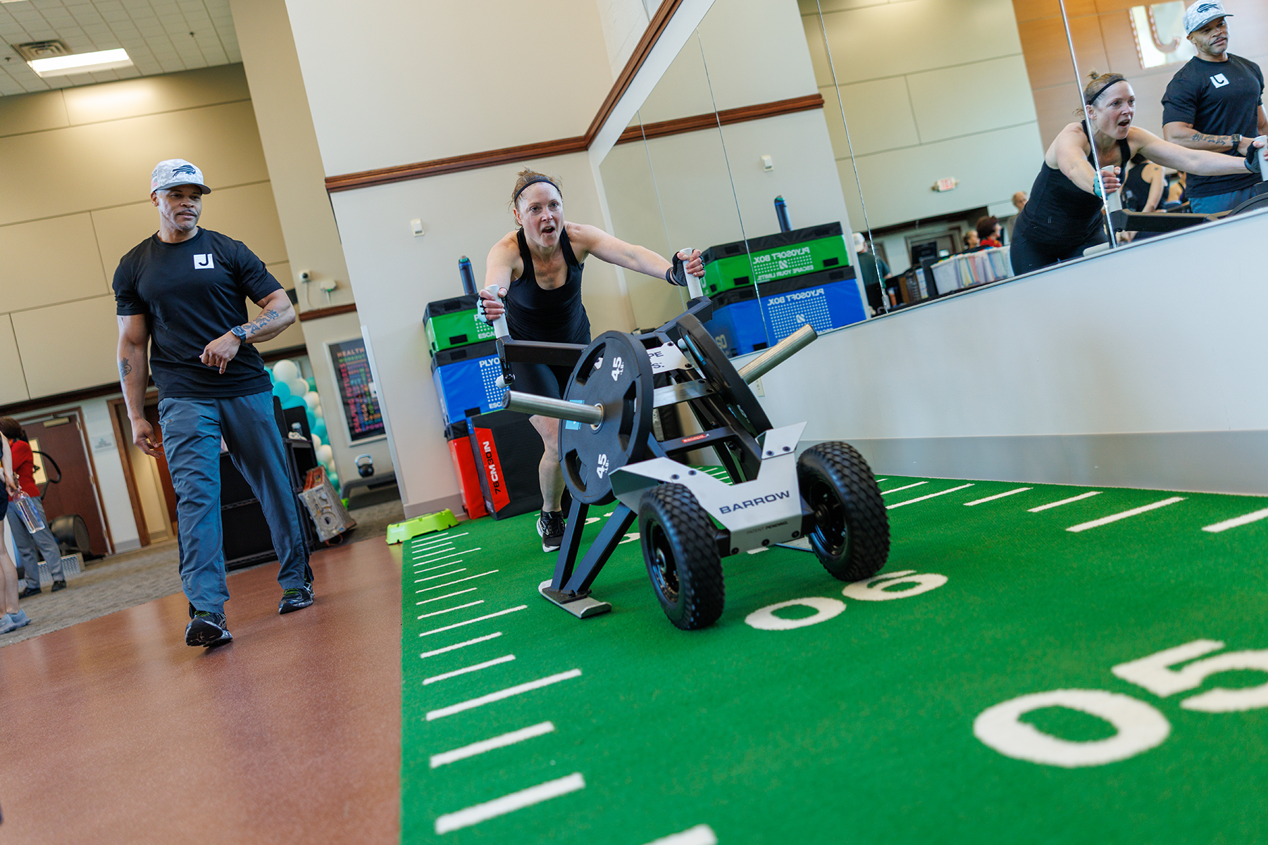 A JCC Buffalo trainer supports a member pushing a weighted exercise sled